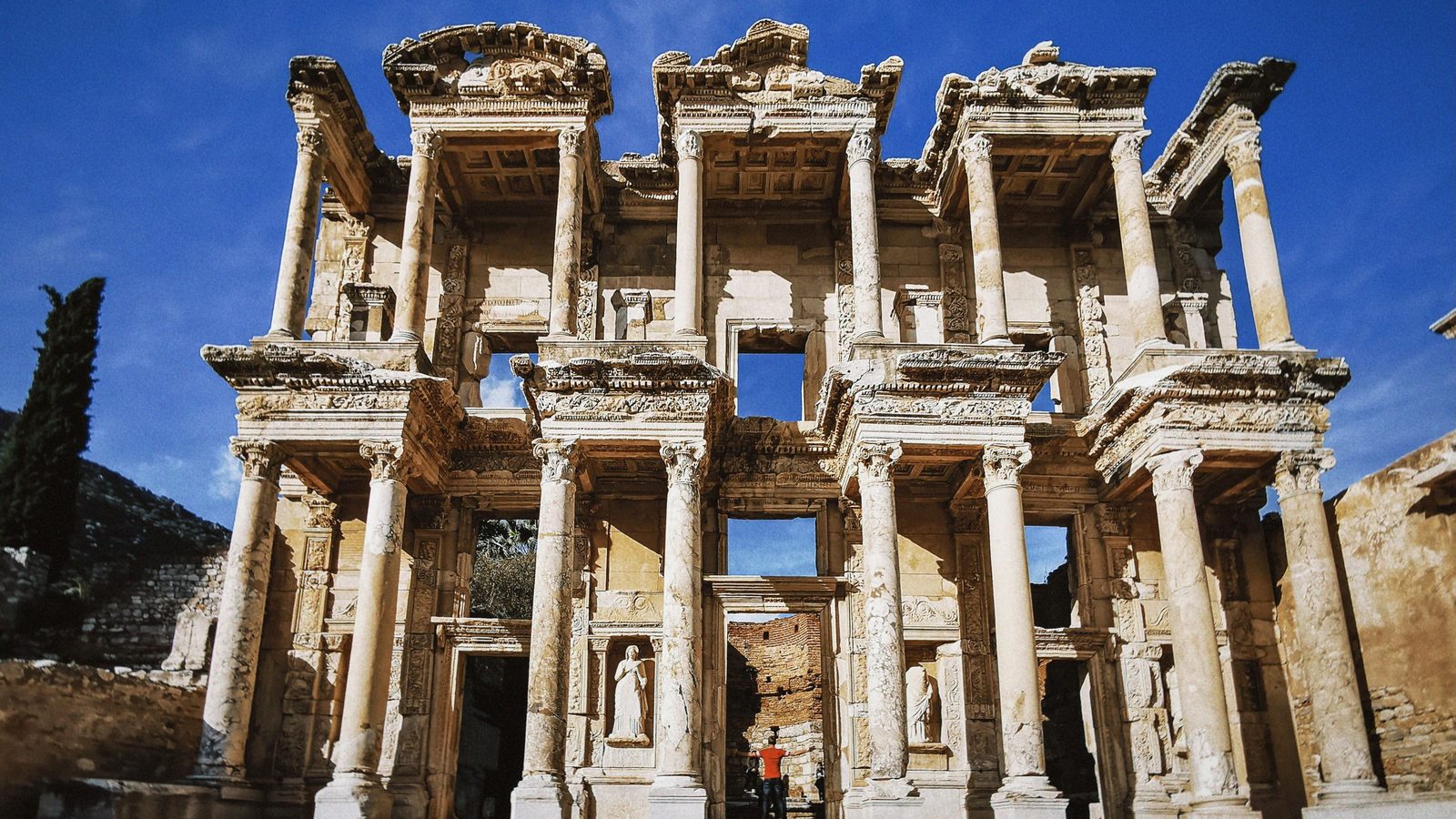The two-story marble facade of the Library of Celsus at Ephesus under a deep blue sky, with statues in its niches