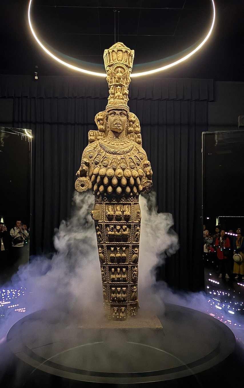 Full-size replica of the Ephesian Artemis statue lit on a circular platform amid drifting mist.