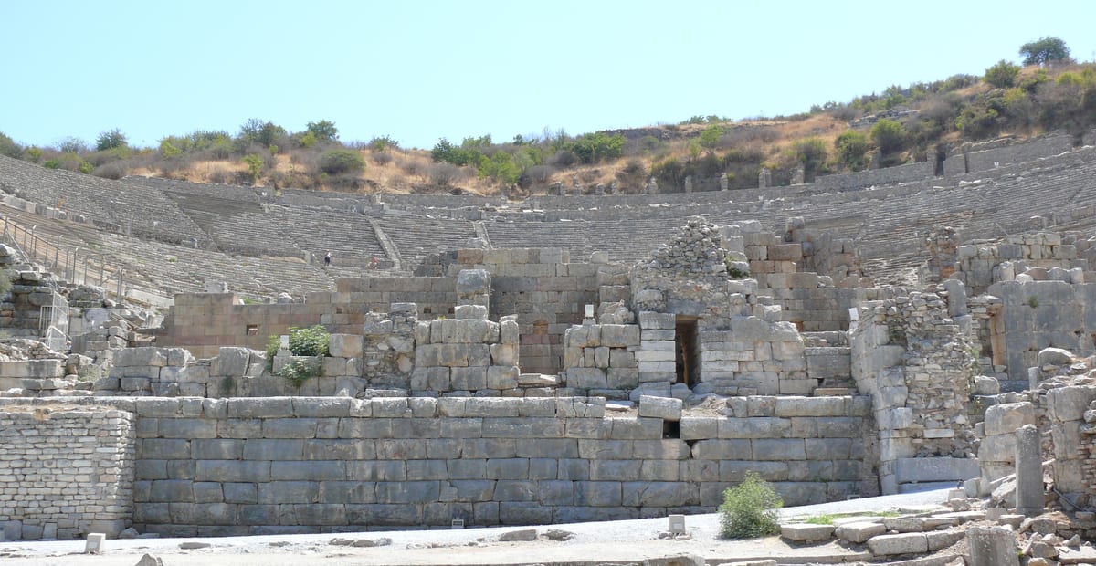 Broken stage walls of the Great Theater of Ephesus with its tiers of stone seats under a clear sky