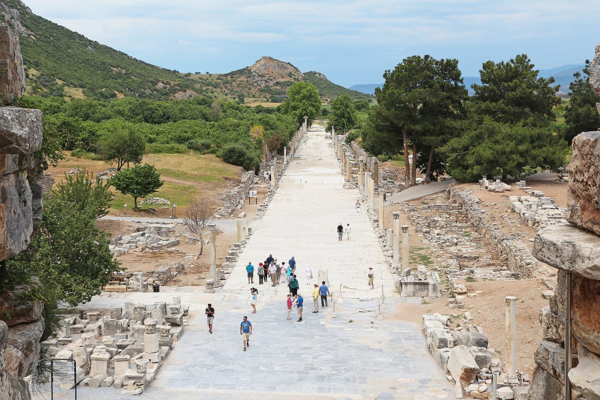 Visitors walking on the marble paving below the Great Theater at Ephesus, with Harbor Street running away toward the valley