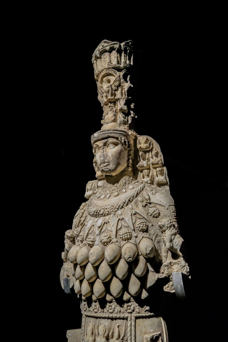 The Great Artemis statue in the Ephesus Museum in Selcuk, lit against a dark background, with her tall tiered crown, damaged face and rows of oval shapes across her chest