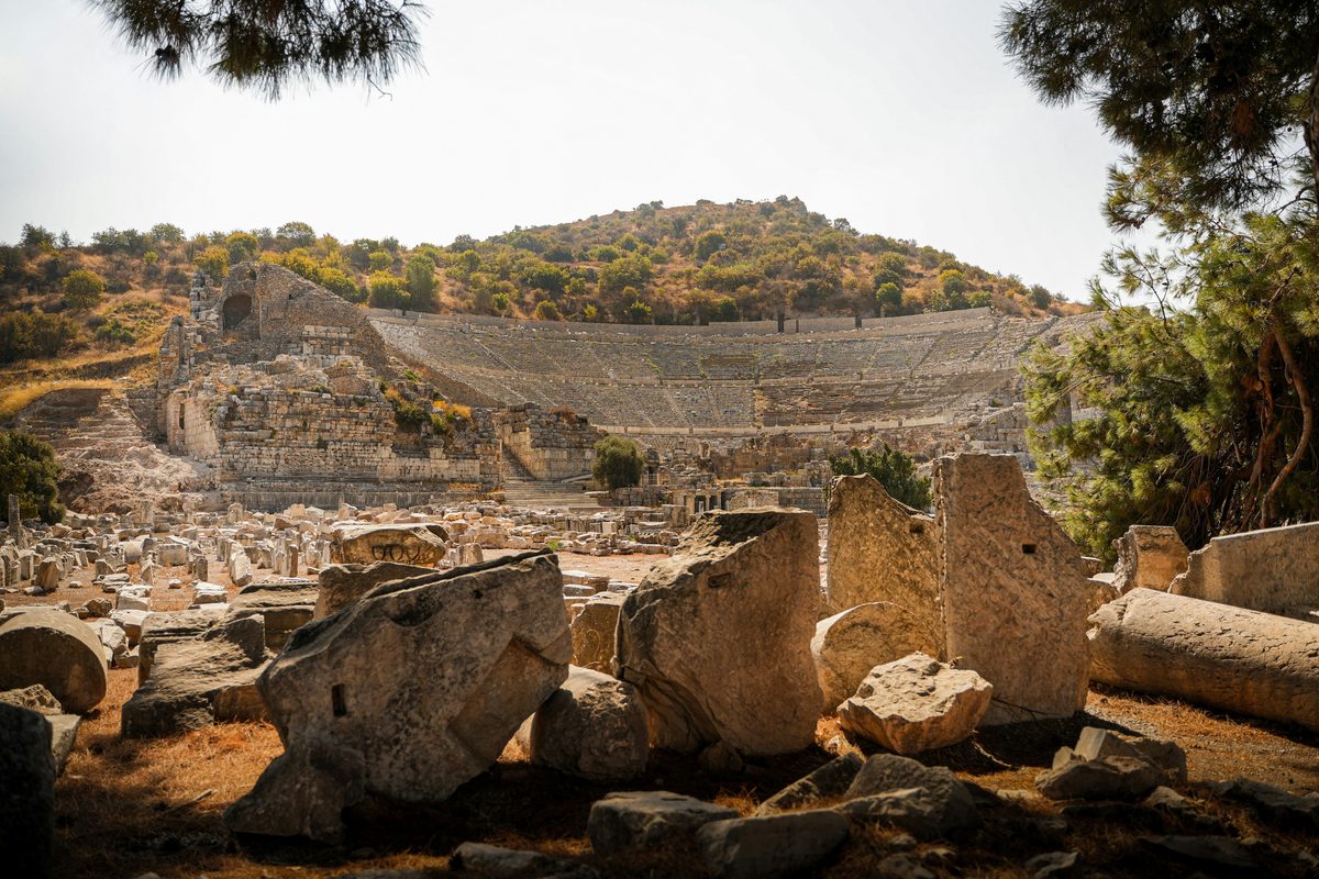 The curved stone seating of the Great Theater at Ephesus cut into a pine-covered hill, seen across scattered marble blocks