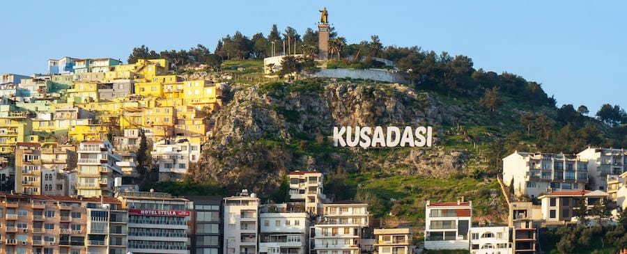 Large white hillside letters spelling KUSADASI above the town's apartment buildings