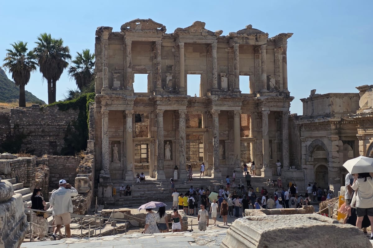 Summer visitors with sun umbrellas filling the square in front of the Library of Celsus at Ephesus