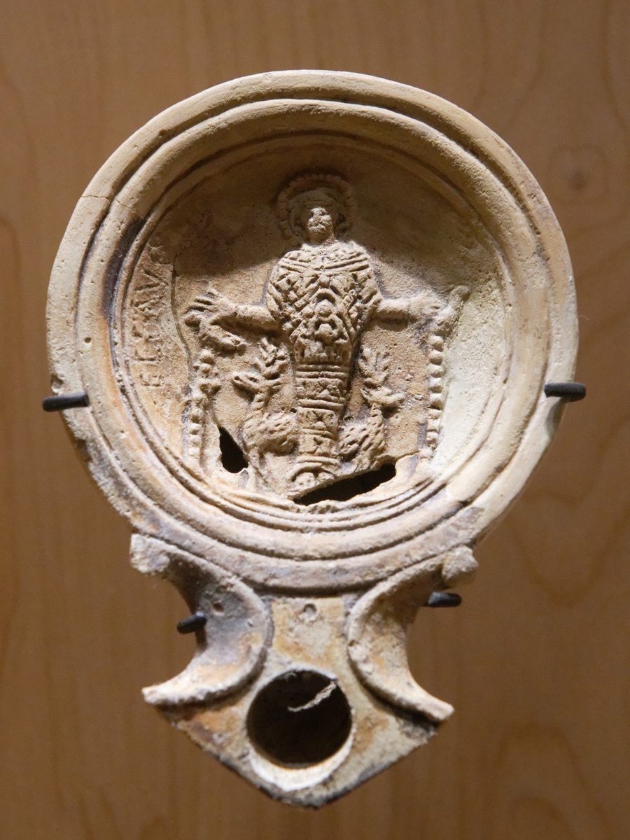 A Roman clay oil lamp with a relief of the Ephesian Artemis standing stiffly between two deer