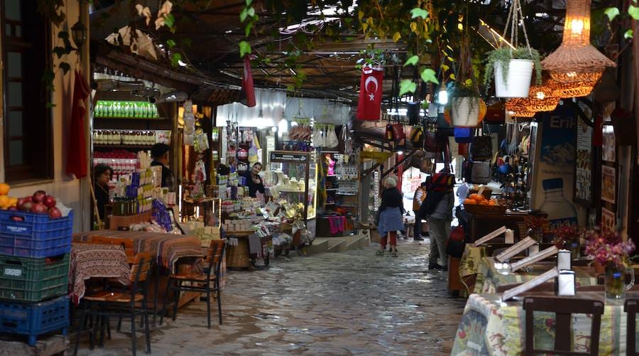 Narrow cobbled lane in Sirince village lined with small shops selling local goods under vines and hanging lanterns.