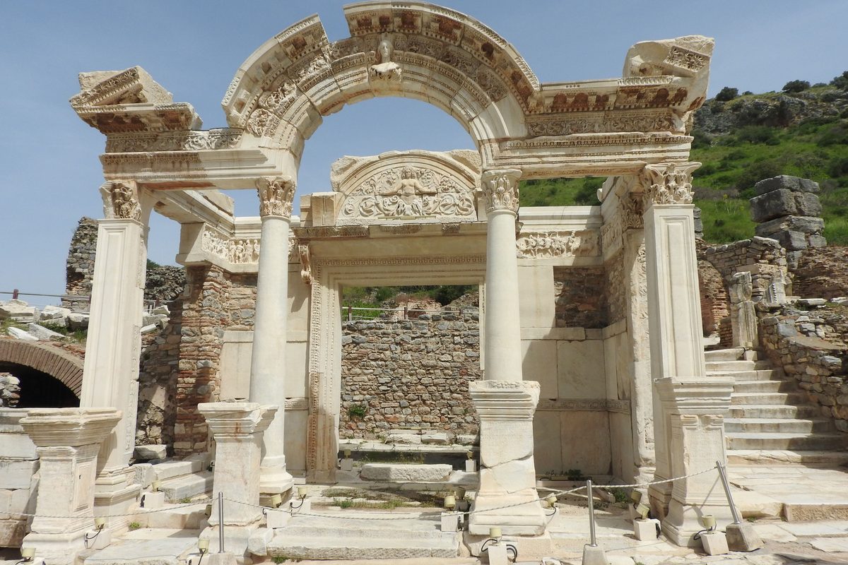 The arched marble front of the Temple of Hadrian on Curetes Street at Ephesus, with carved reliefs and a green hillside behind