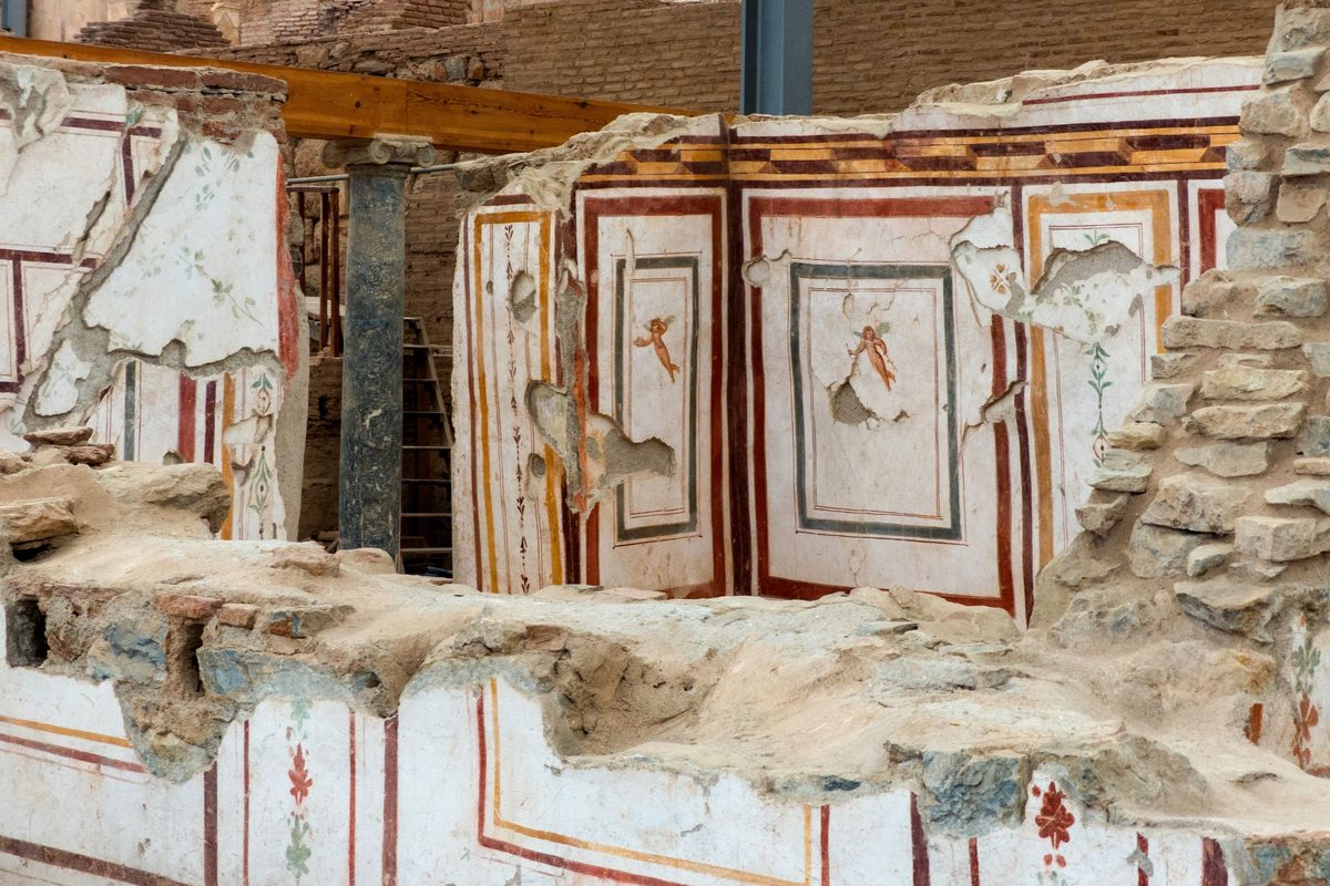 Painted walls inside the Terrace Houses at Ephesus, with red and ochre panels and small flying cupids, under a modern protective roof