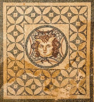 Roman floor mosaic showing a winged Medusa head in a round medallion framed by an interlocking circle pattern.